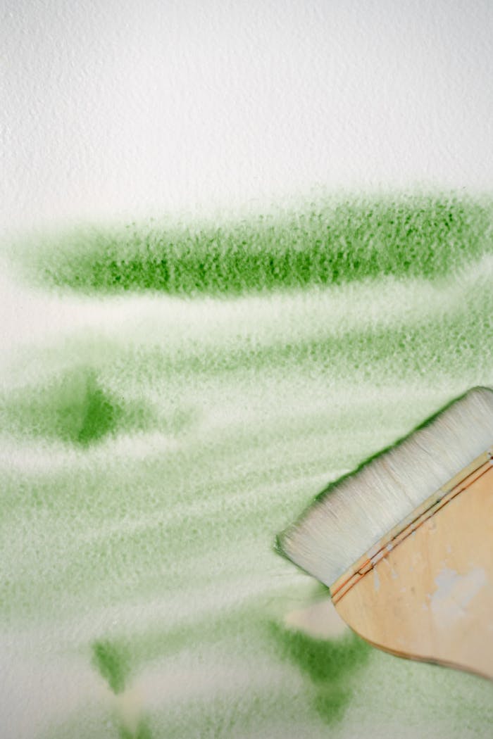 Green watercolor brushstroke on canvas with paintbrush illustrating artistic texture.