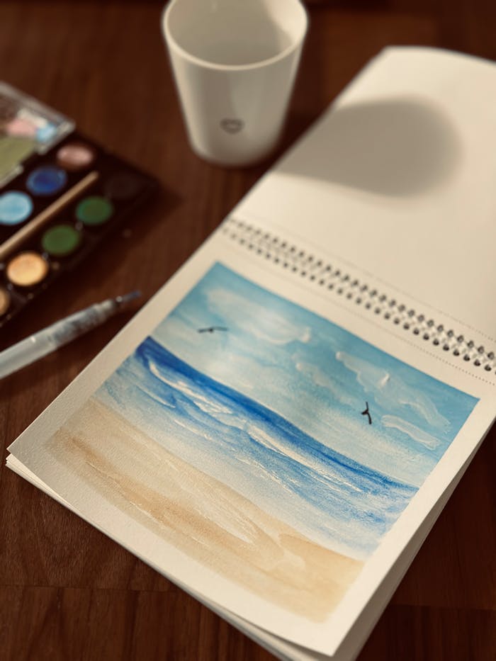 Peaceful watercolor seascape painting with art supplies on a wooden table.
