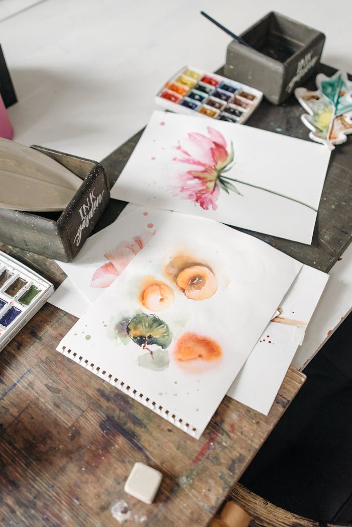 Artistic workspace featuring watercolor paintings and art supplies on a wooden table.
