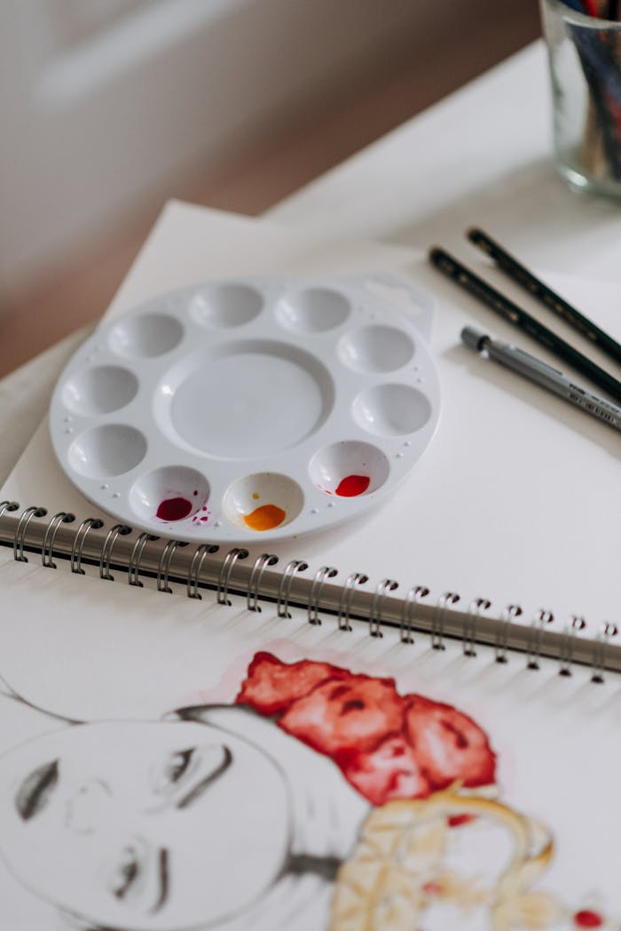 Creative workspace featuring a watercolor palette with a drawing in progress and brushes on a desk.